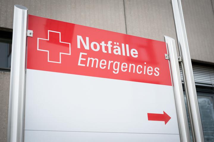 Rot-weißes Schild mit Krankenhaus-Kreuz und der Aufschrift “Notfälle”, darunter steht “Emergencies” und ein Pfeil