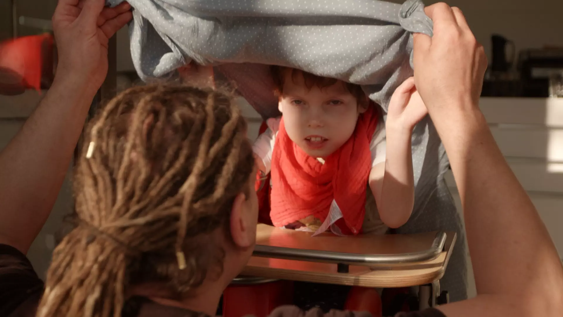 Ein kleines Kind schaut aus einer Decke hervor. Das Bild zeigt eine Szene aus der Serie "Elternabend".