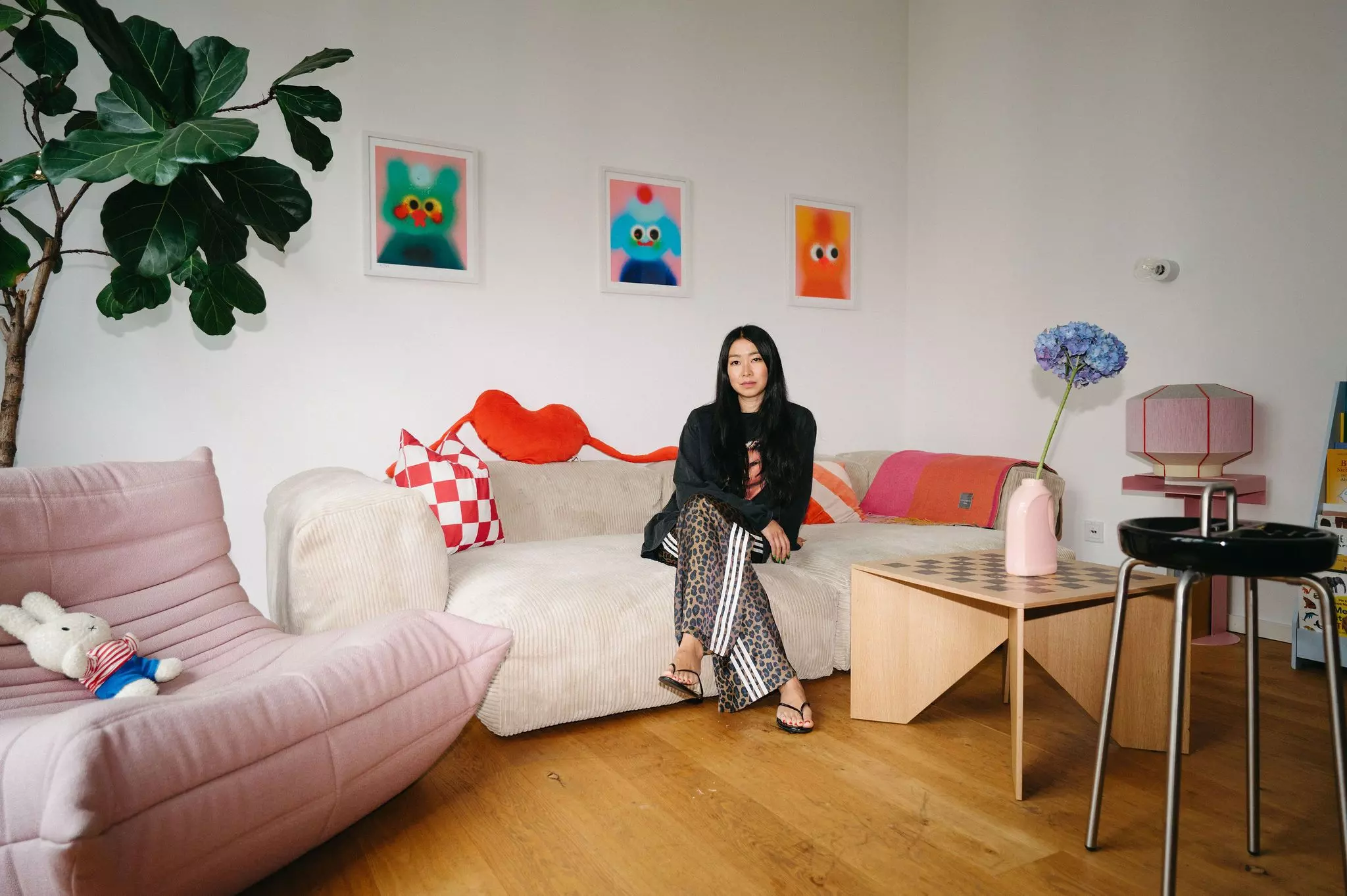 Homestory Ubin Eoh: Die Autorin sitzt auf einem großen Sofa, über dem drei bunte Bilder des Künstlers Jon Burgerman hängen.