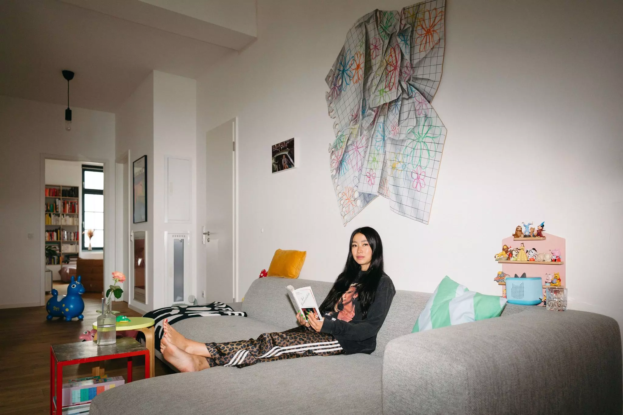 Homestory Ubin Eoh: Die Autorin sitzt auf ihrem Sofa, liest in der Anthologie "Die Damentoilette", über dem Sofa hängt ein Kunstwerk von Johannes Ehemann.