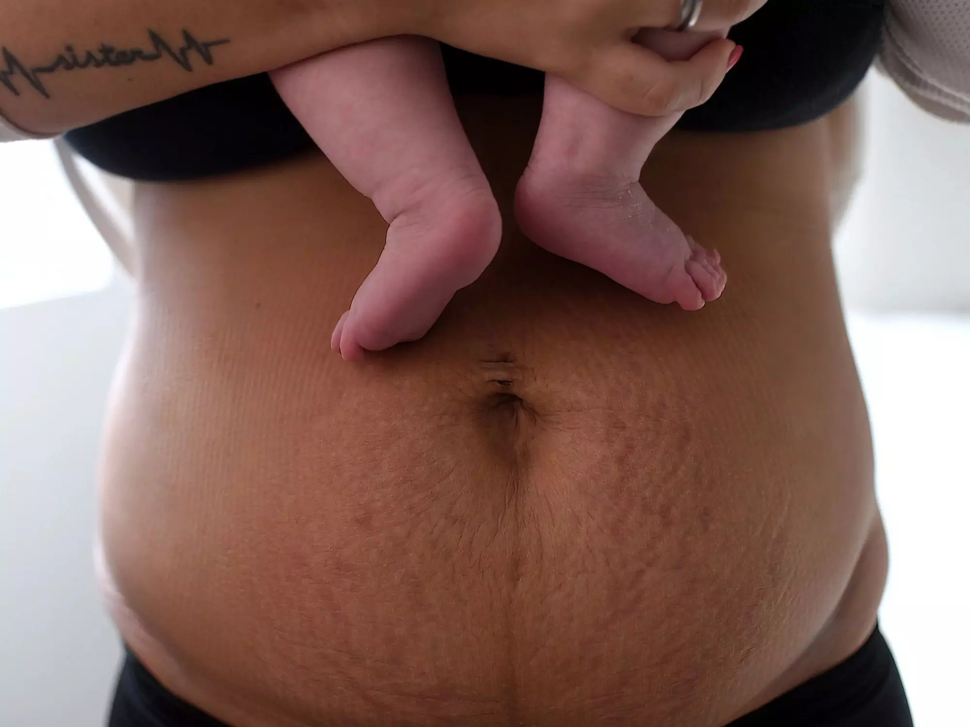 Babyfuesse vor einem Bauch als Symbolbild fuer das Tabu, ehrlich ueber den Koerper der Mutter nach der Geburt zu sprechen