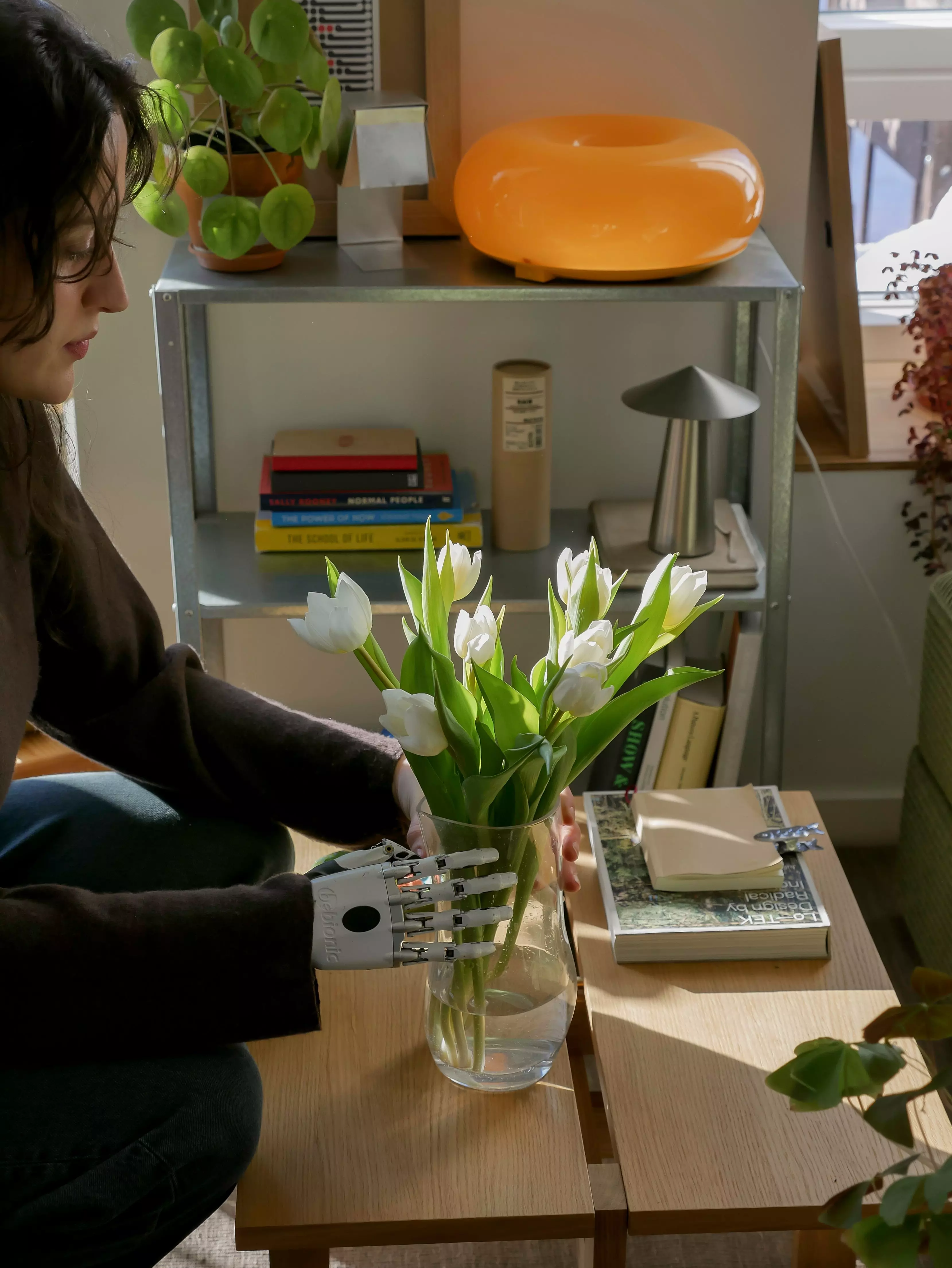 Architektin und Möbeldesignerin Lara Joy arrangiert einen Strauße weißer Tulpen in einer Glasvase auf ihrem Wohnzimmertisch.