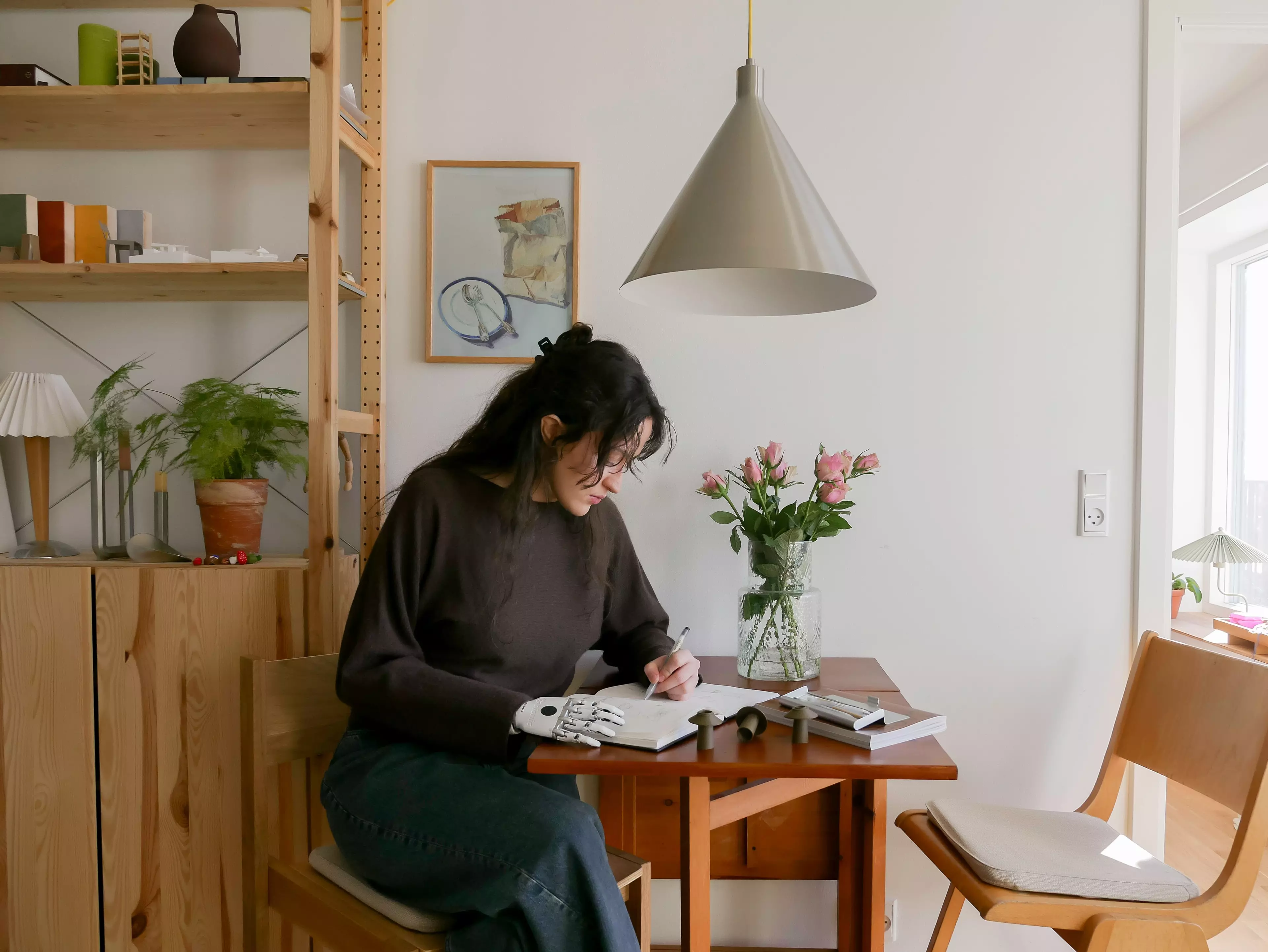 Architektin und Möbeldesignstudentin Lara Joy sitzt an ihrem Esstisch und zeichnet in ein Skizzenbuch.