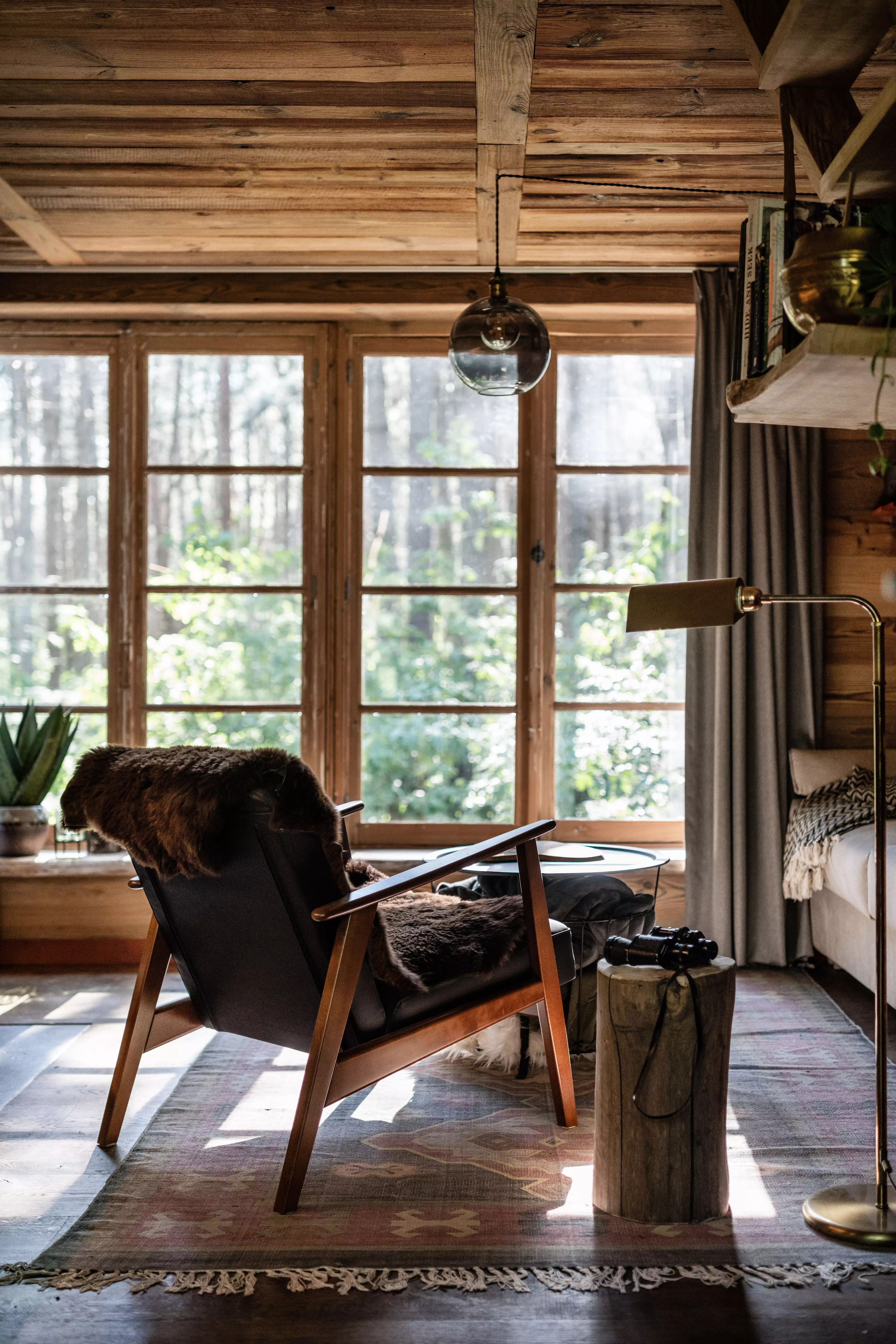 Wohnbereich im Inneren eines Baumhauses der Treelodge in Belgien, ein Sessel der vor einer grossen Fenstertuer steht.