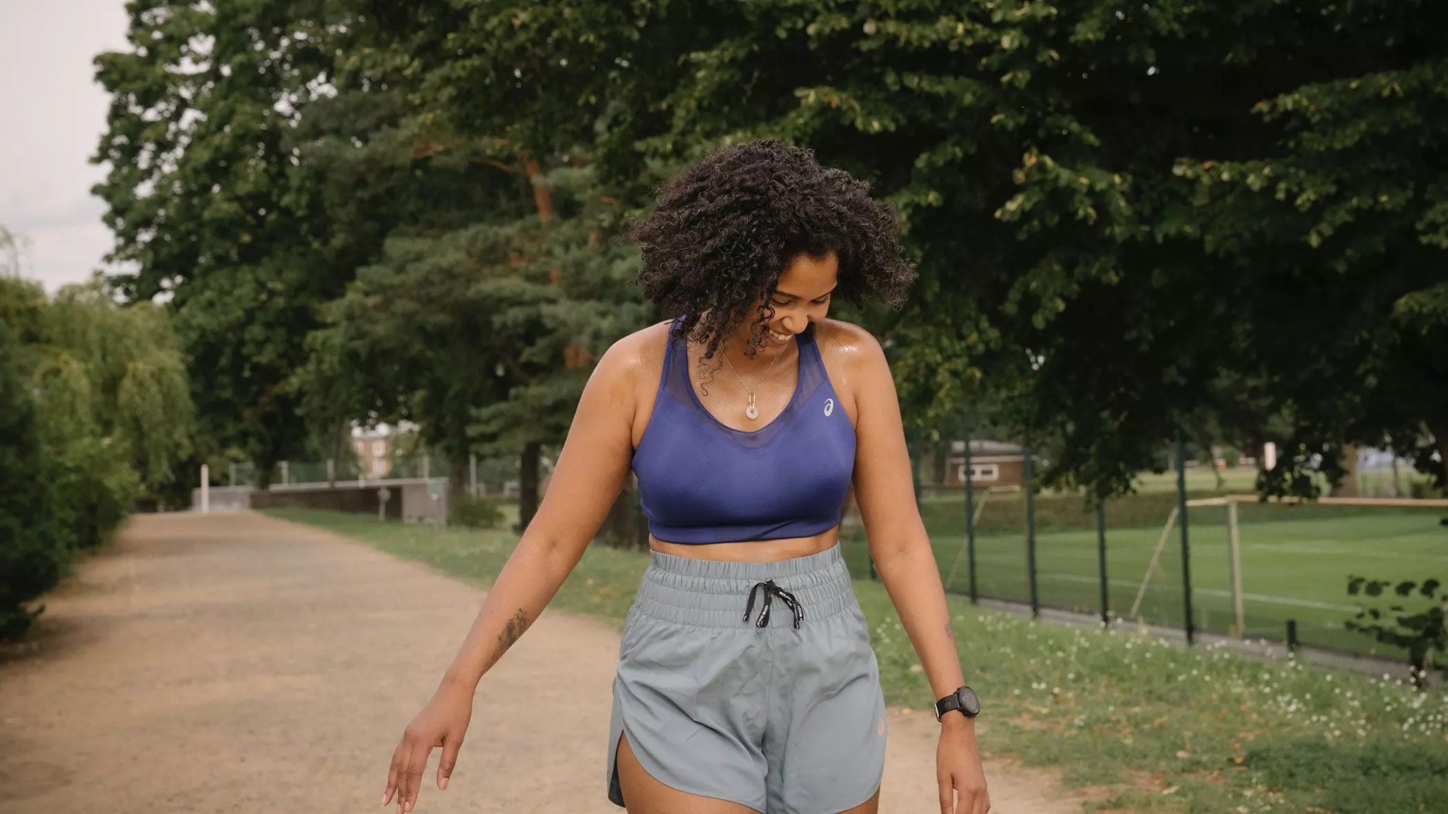 Frau mit Afro in Sport-Bra und Sport-Shorts auf einem Weg vor Bäumen – femtastics
