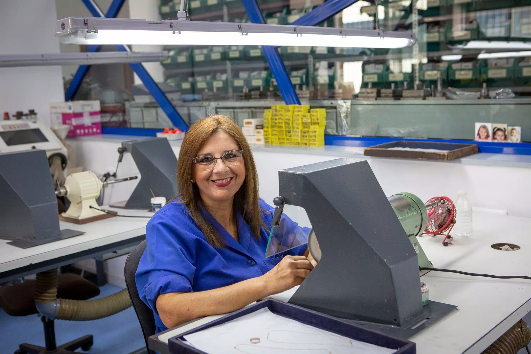 Eine blonde Frau mit einer Brille und einem blauen Oberteil sitzt lächelnd an einer Werkbank – femtastics