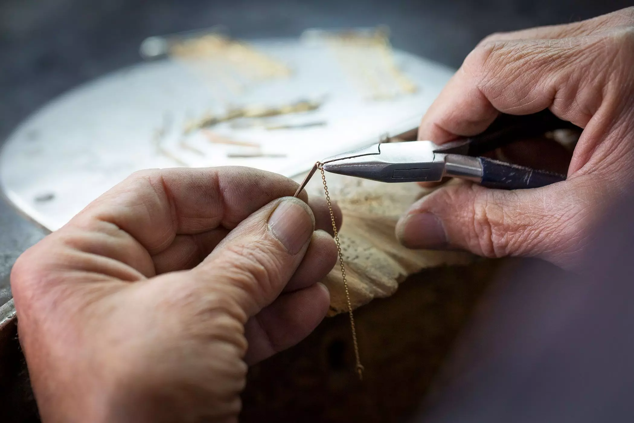 Hände, die mit einem Werkzeug an einer zarten Goldkette arbeiten – femtastics