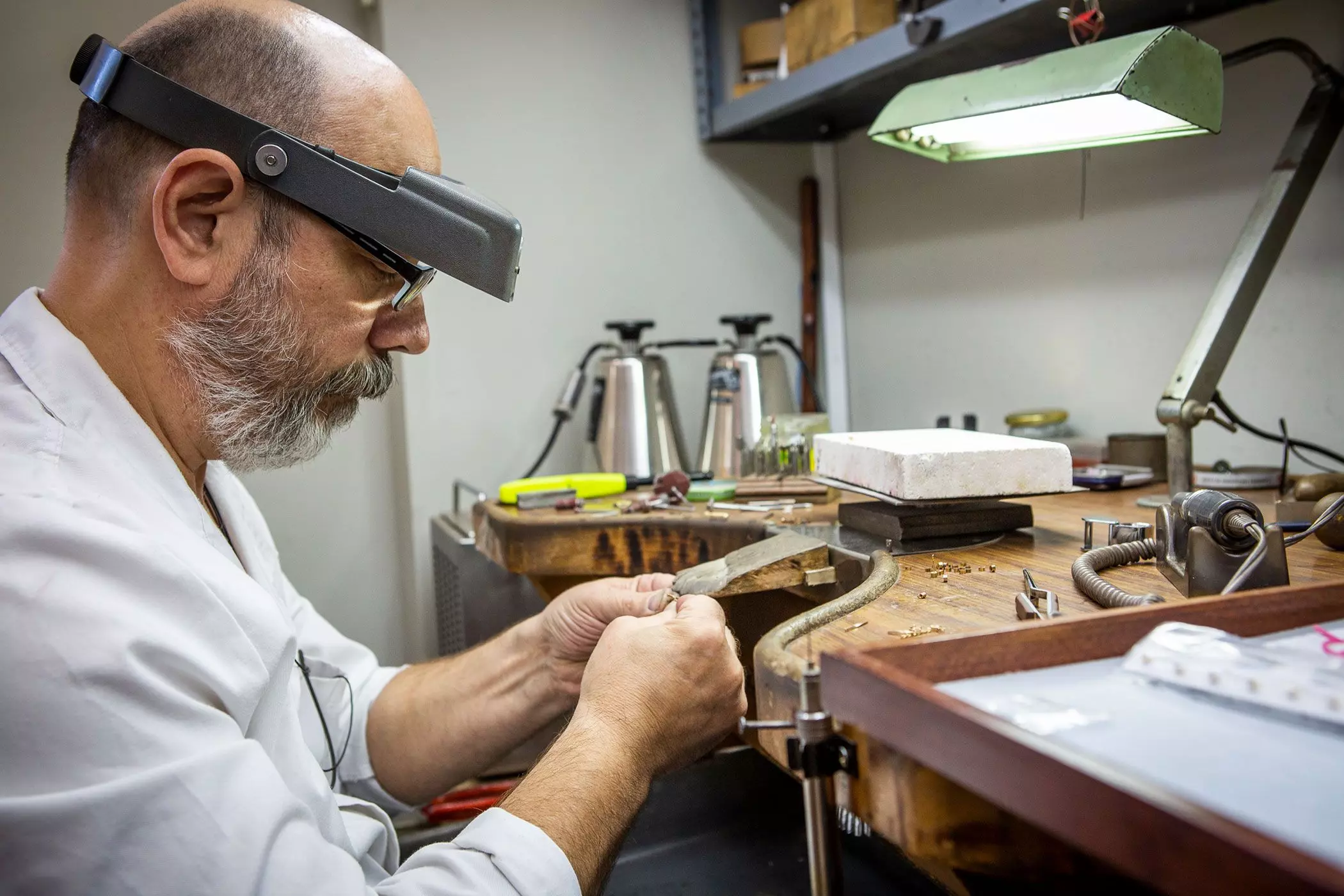 Ein bärtiger Mann mit einer Spezialbrille arbeitet in einer Werkstatt an Schmuckstücken - femtastics