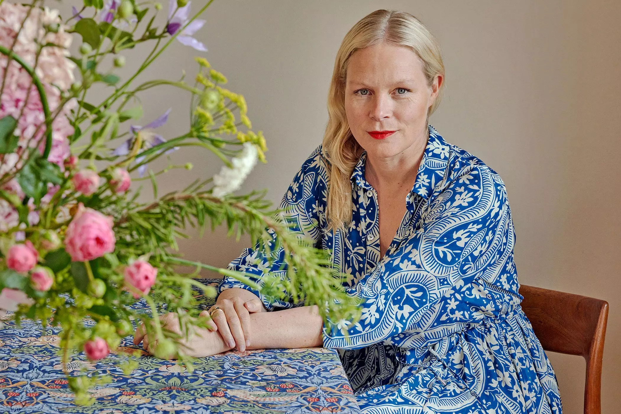 Anne Petersen in einem blauen gemusterten Kleid neben einem Blumenstrauß