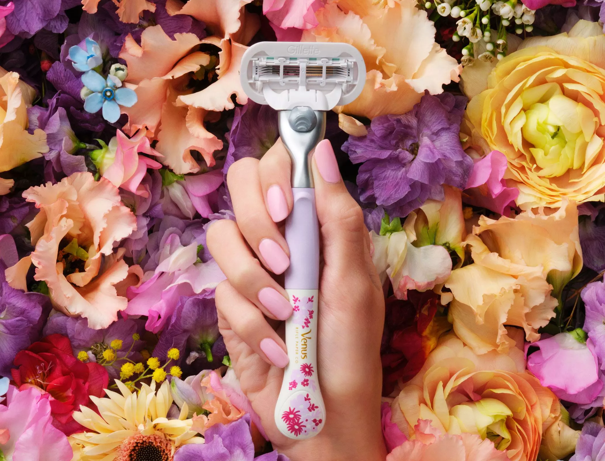 Weibliche Hand hält einen Gillette Venus Rasierer, umgeben von Blüten