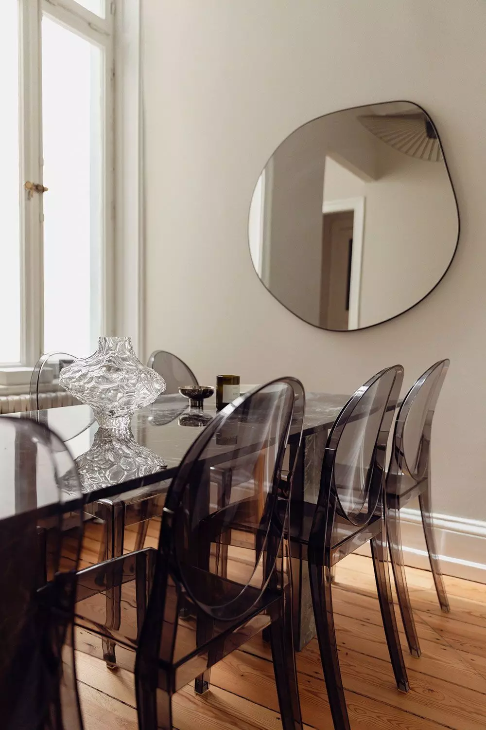 Esstisch mit Plexiglasstühlen und rundem Spiegel an der Wand im Hintergrund