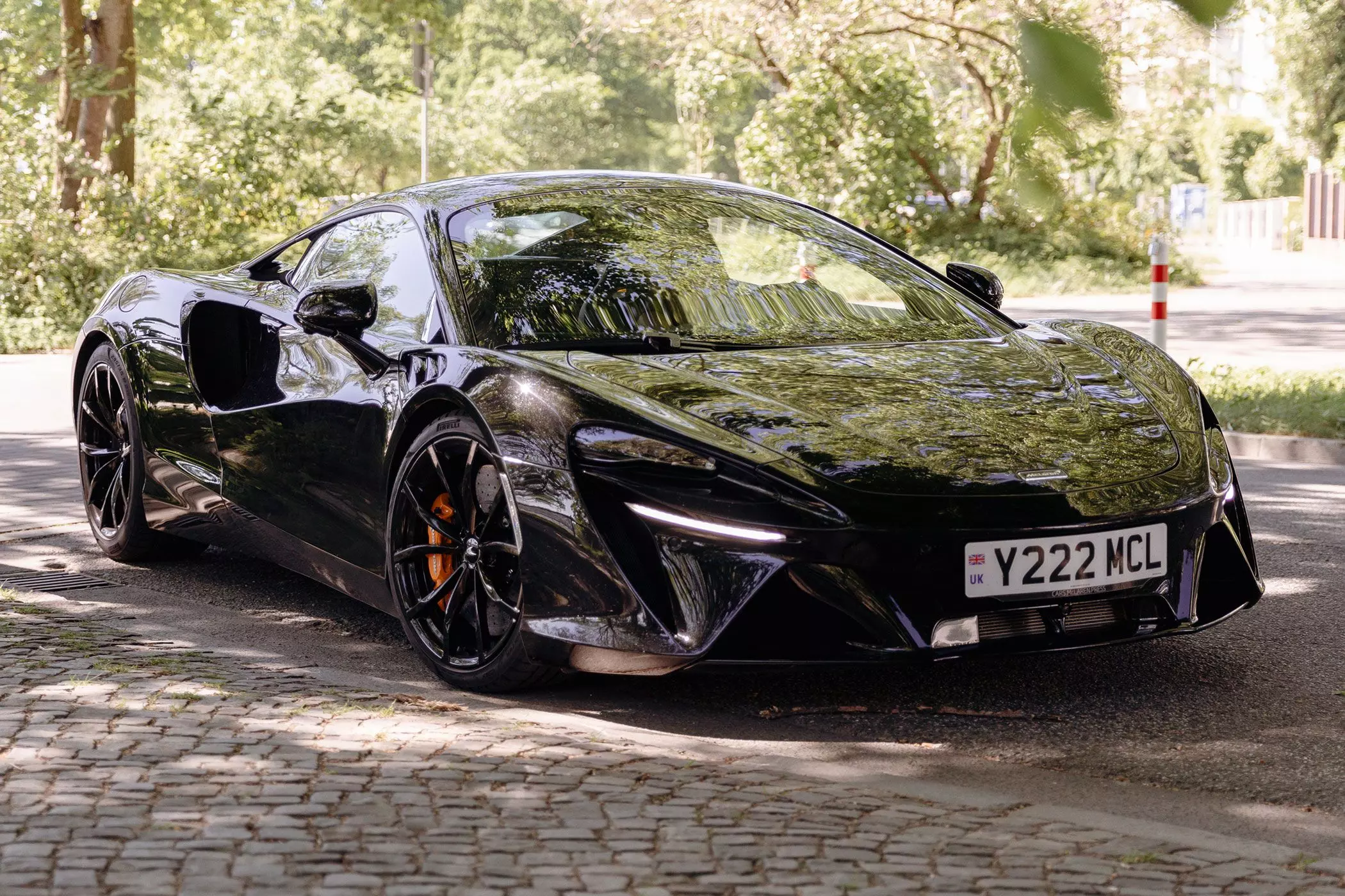 Schwarzer McLaren Artura vor grünen Bäumen