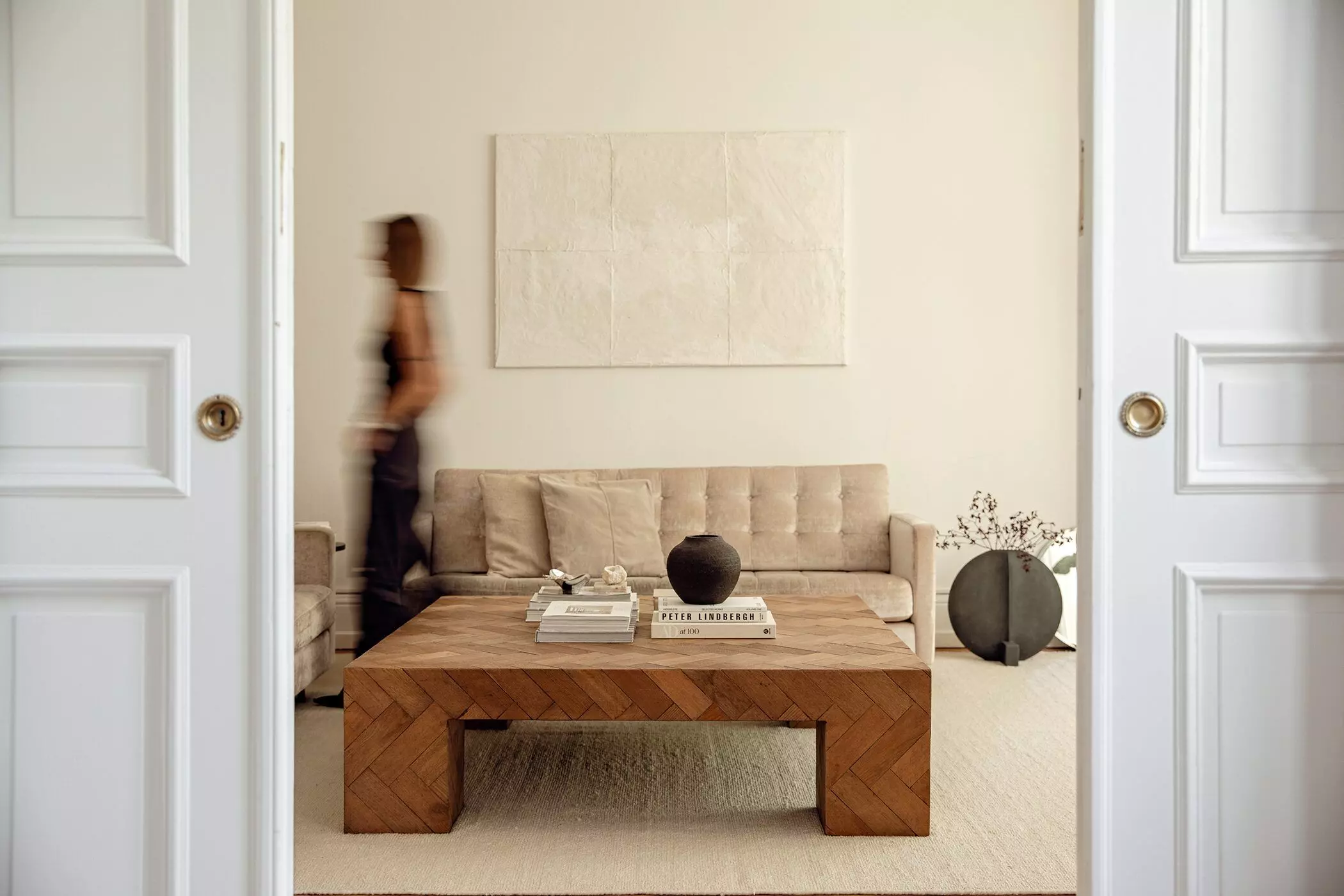 Wohnzimmer mit Holztisch und beigem Sofa in einem Altbau mit Flügeltür