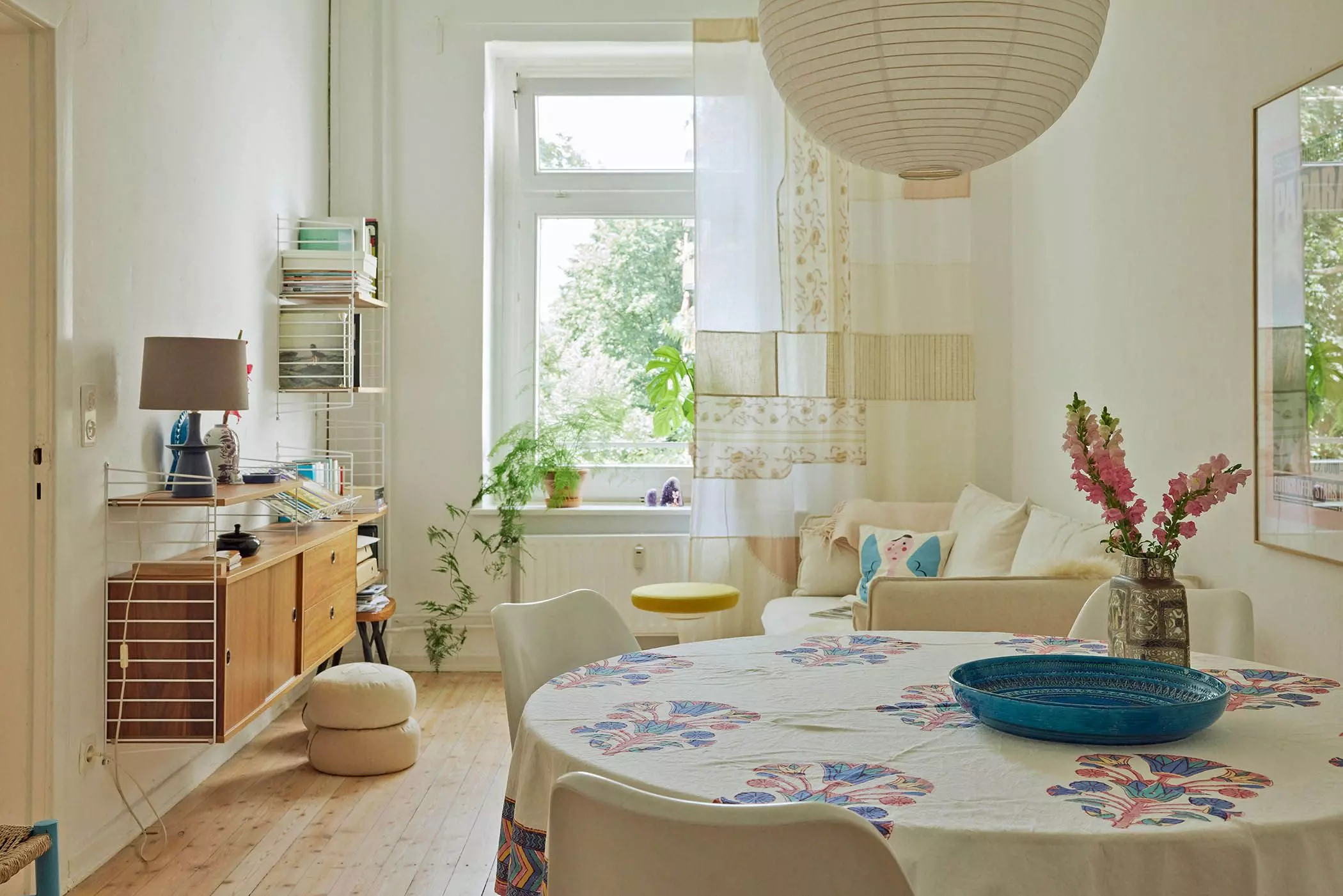 Helles Wohnzimmer mit Esstisch, Wandregal und Sofa mit Patchwork-Gardine vor einem Fenster - femtastics