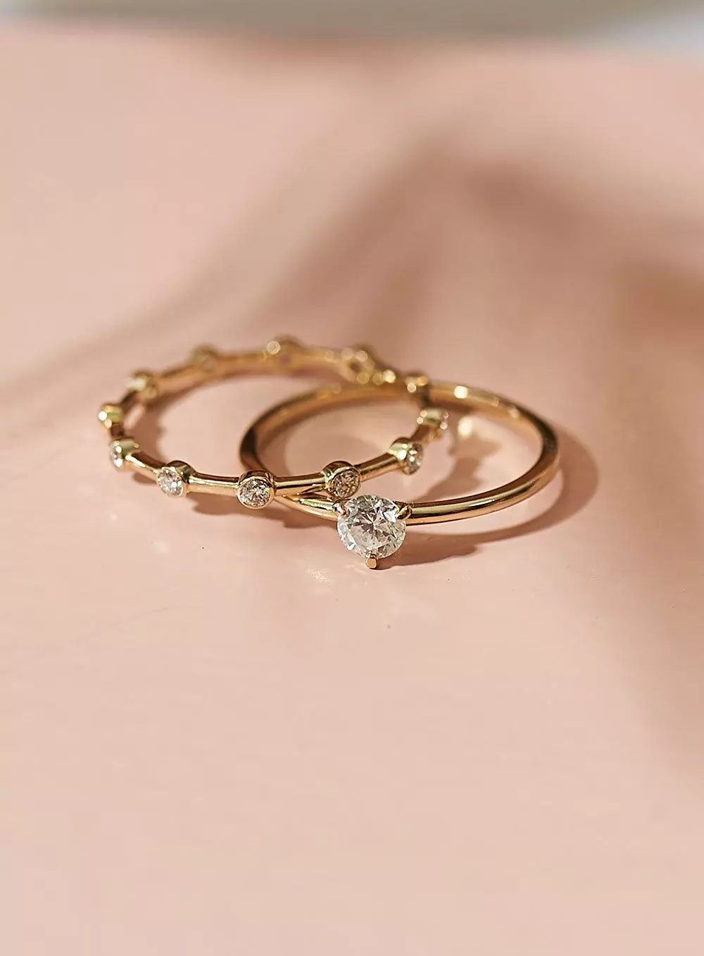 Zwei Goldringe – ein schmaler mit vielen kleinen Diamanten und einer mit größerem Solitaire-Diamant – auf weißem Untergrund – femtastics