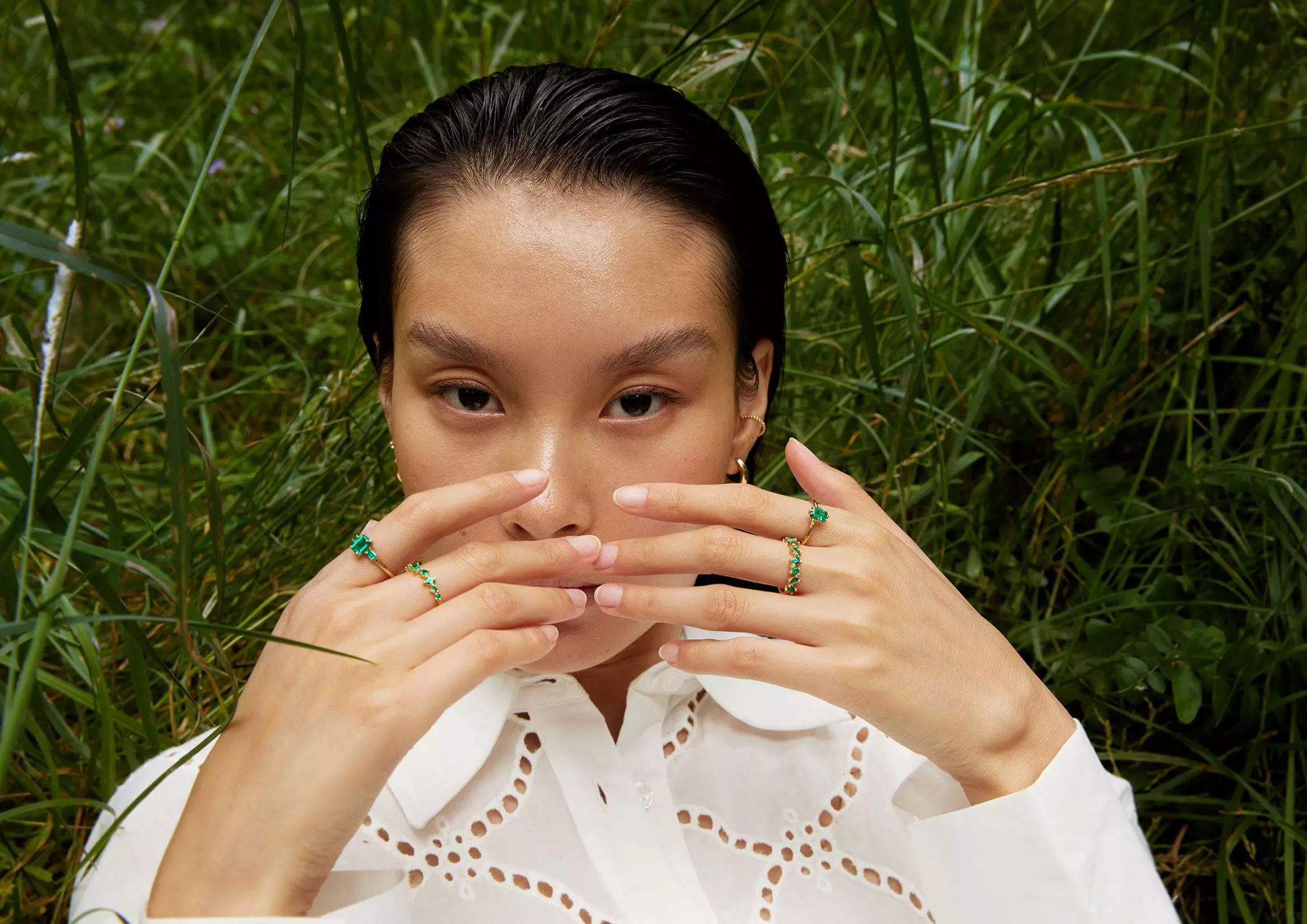 Frau mit smaragdbesetzen Ringen an den Fingern liegt auf einer Wiese – femtastics