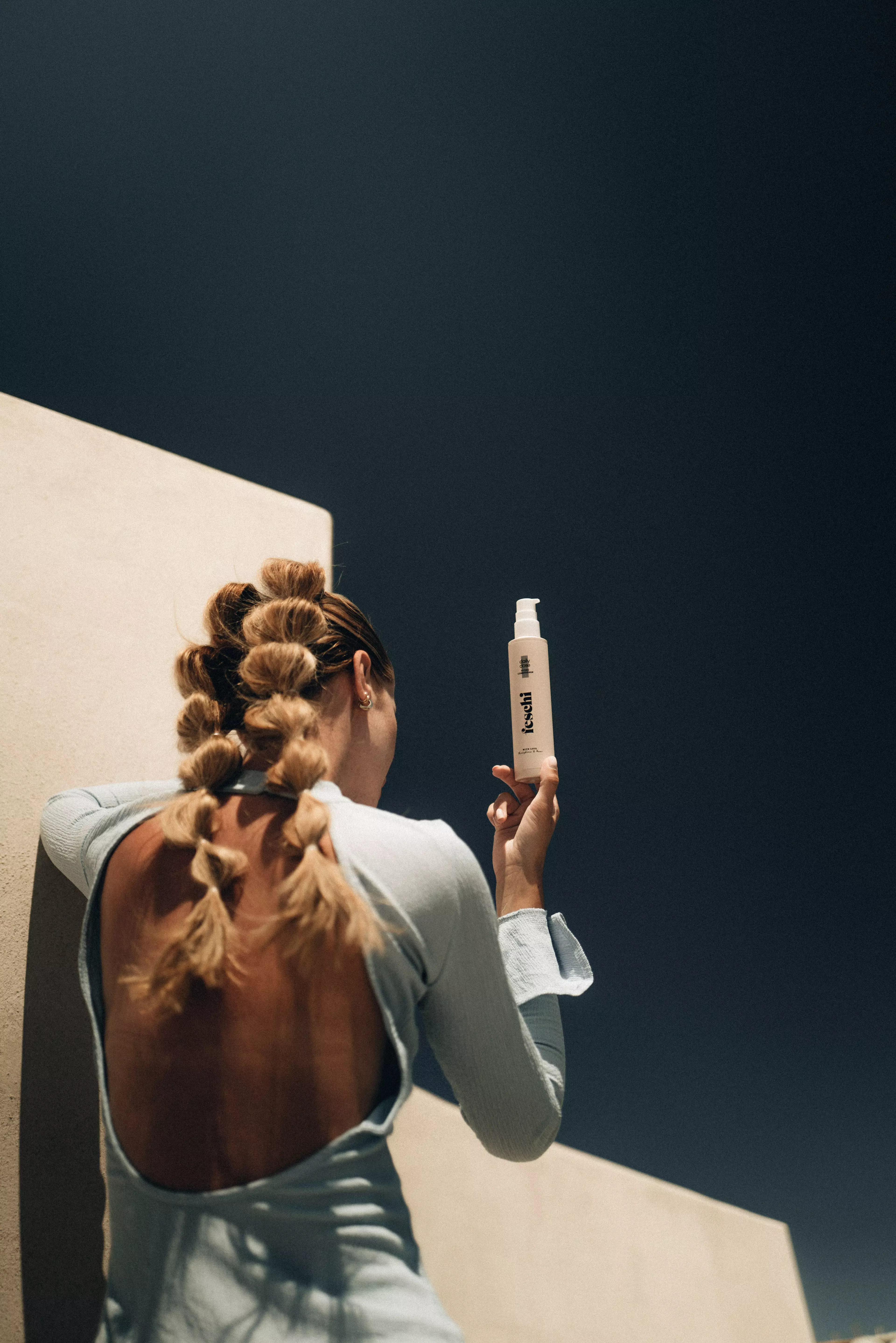 Foto einer Frau mit zwei kunstvollen Zöpfen, die Haarpflege der Marke "feschi" hält.