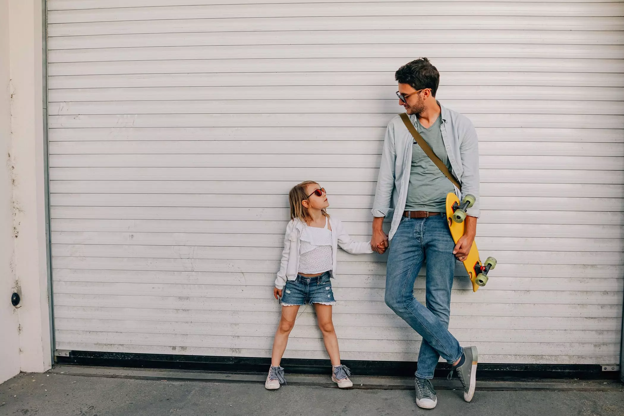 Vater mit Skateboard hält Tochter an der Hand - femtastics