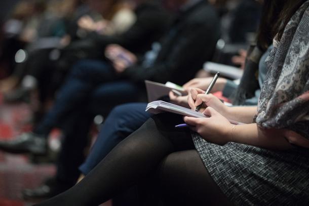 Teilnehmer einer Fachkonferenz notieren sich etwas in Notizheften