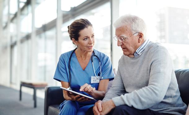 Eine Krankenschwester erläutert einem älteren Herren auf einem Tablet das geriatrische Assessment