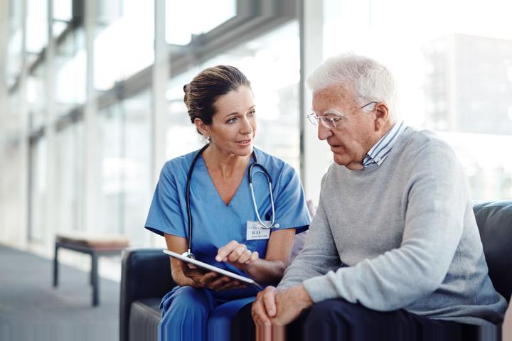 Eine Krankenschwester erläutert einem älteren Herren auf einem Tablet das geriatrische Assessment